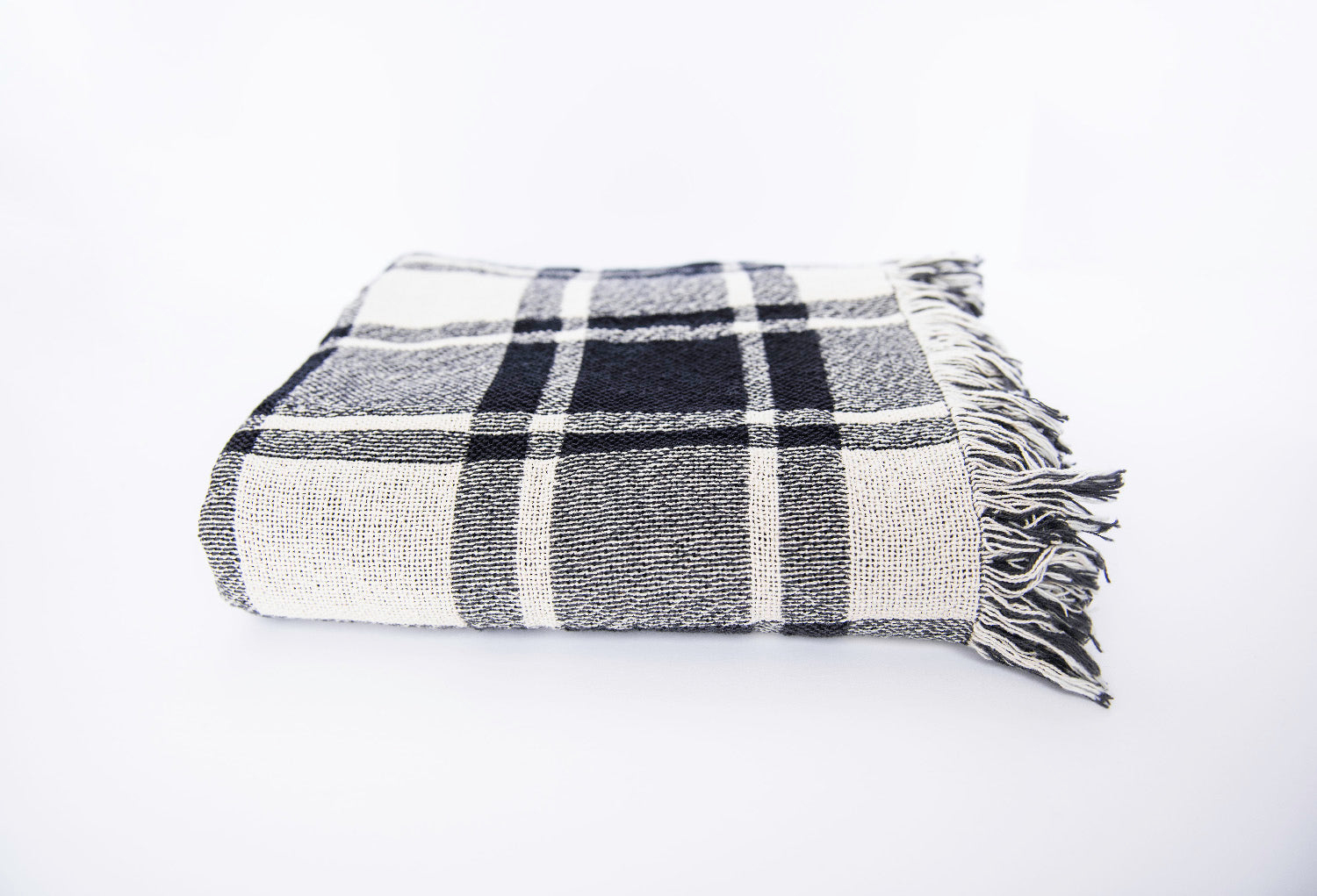 Front view of folded black, gray, and cream plaid woven cotton throw on a white background