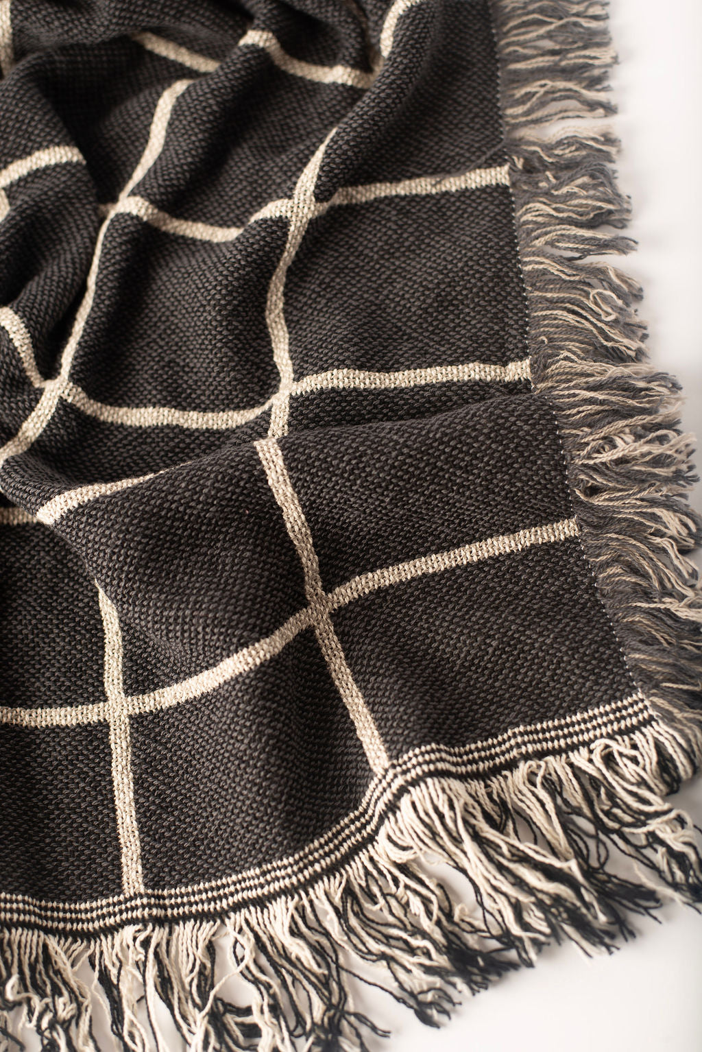 Close-up of Greer Nocturne charcoal and cream grid woven cotton throw blanket with fringe