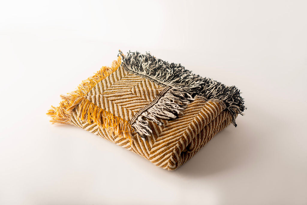 Woven blanket with herringbone pattern and fringe on a white background