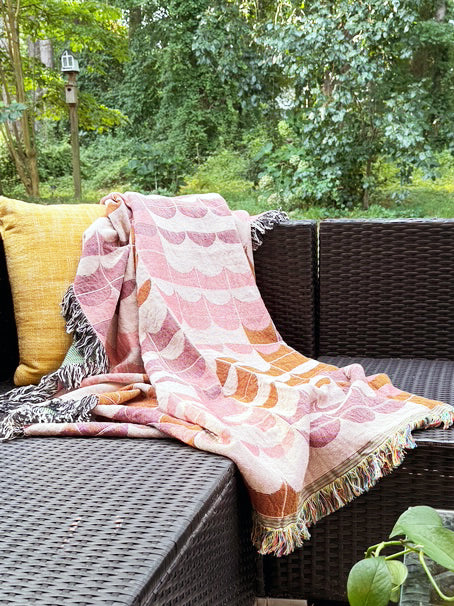 Quinn Blush pink and coral geometric throw blanket draped over an outdoor wicker sofa