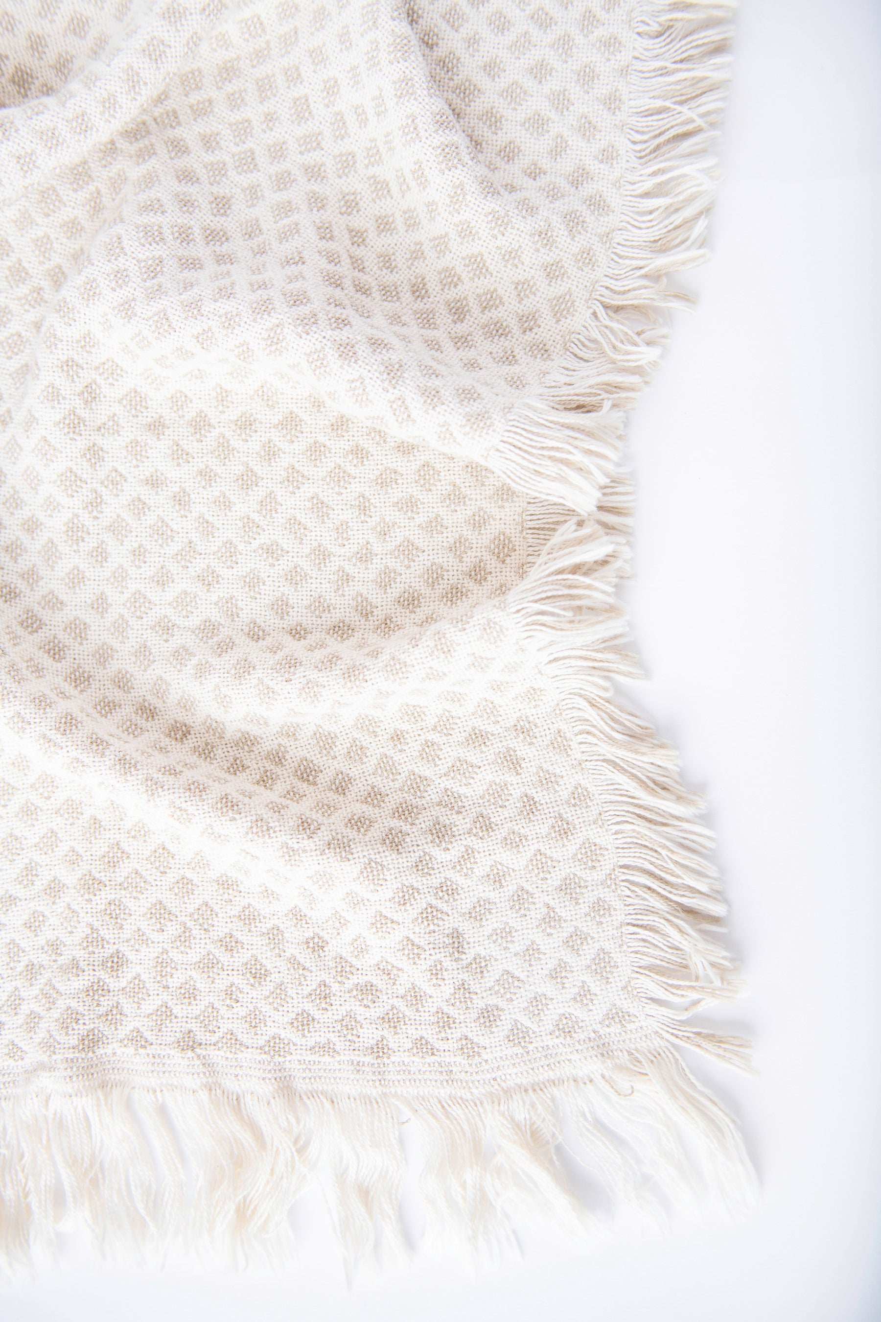 Close-up of Rowan cream and beige diamond-patterned woven cotton throw with neutral fringe