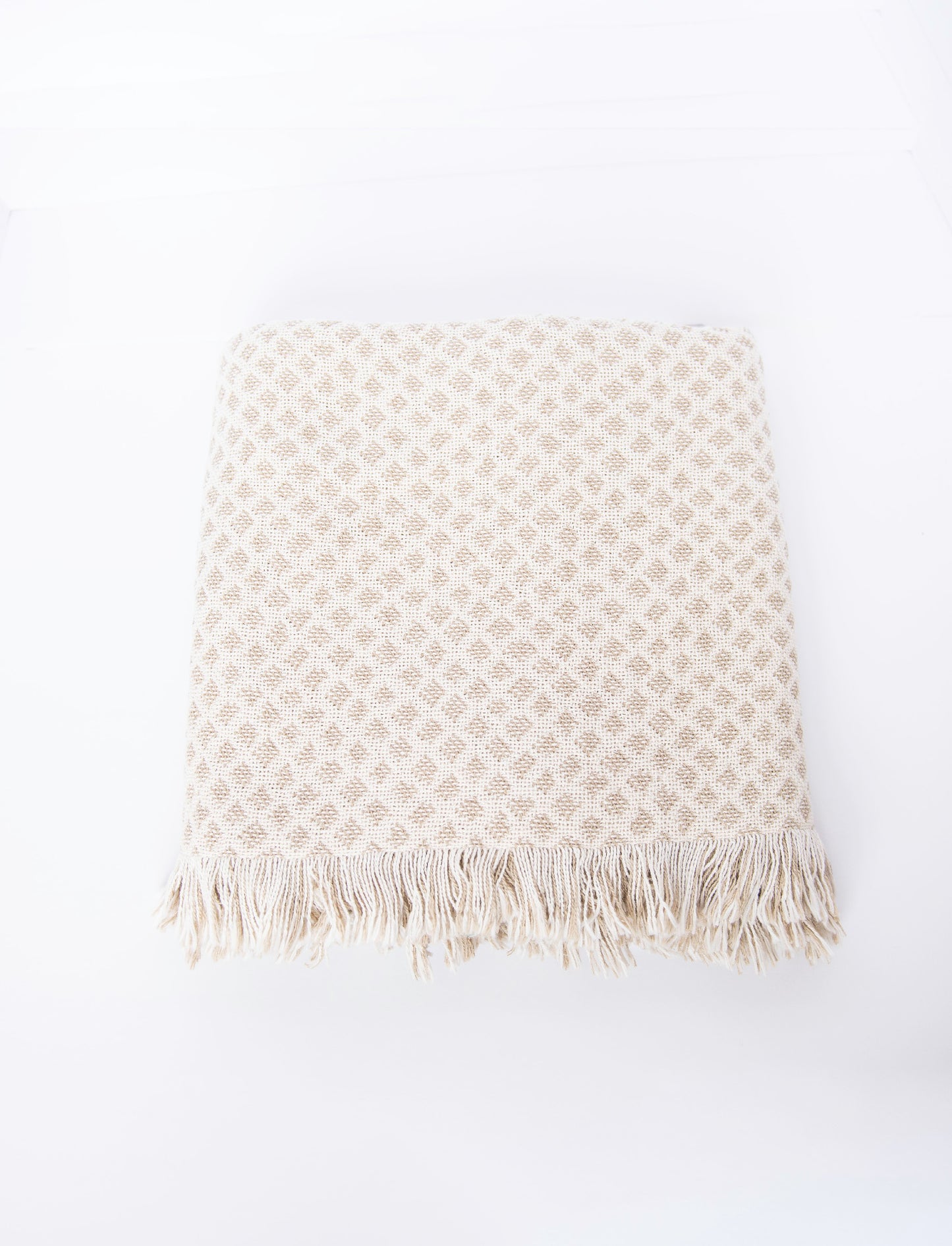 Rowan neutral diamond throw in a stack of colorful Kindly Woven cotton blankets