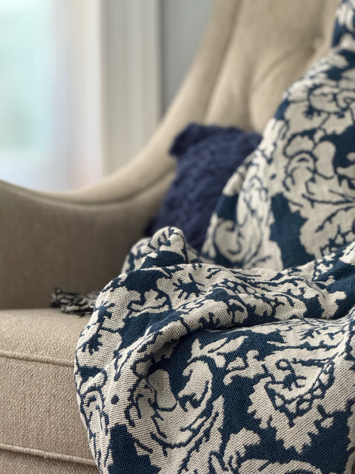 Verona Cerulean blue damask floral throw blanket draped over an upholstered sofa beside a navy pillow