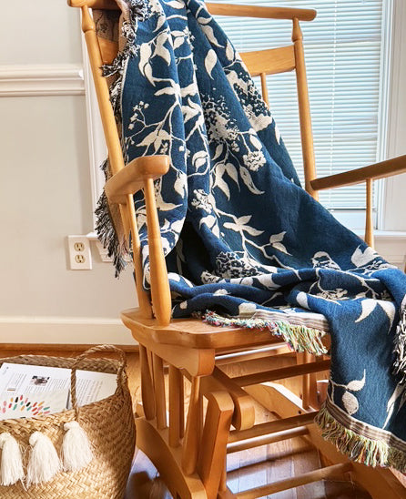 Wren Tidesong bird and botanical throw blanket draped over a wooden rocking chair