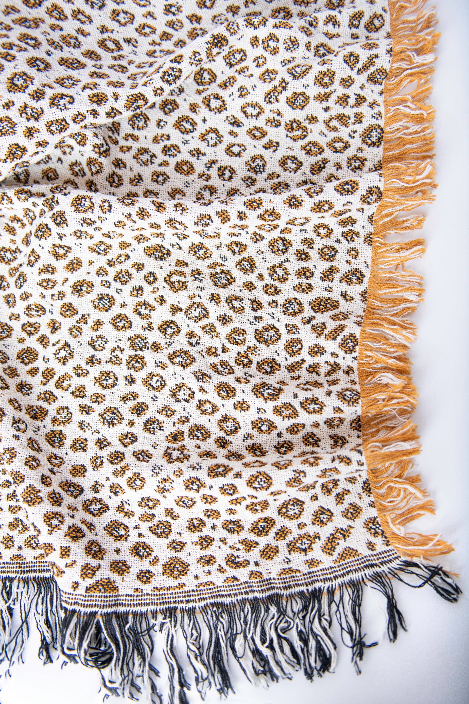 Close-up of Zola golden ochre, black, and cream leopard-print woven cotton throw with fringe
