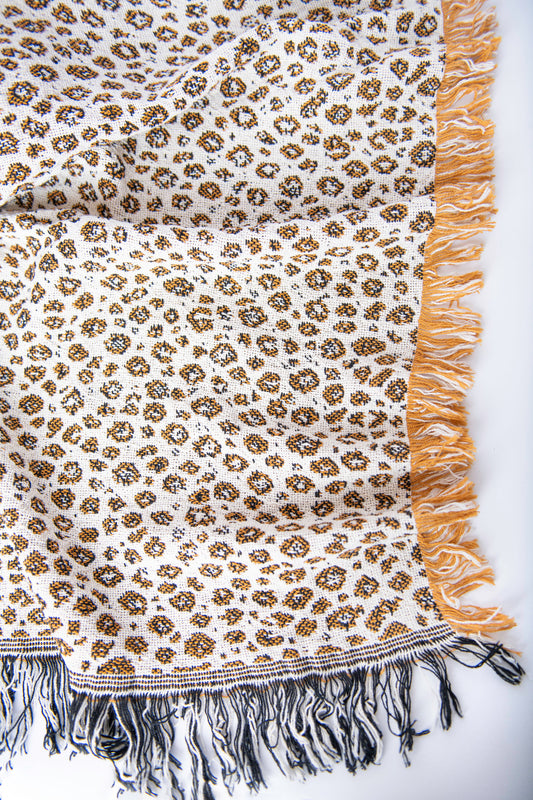 Close-up of Zola golden ochre, black, and cream leopard-print woven cotton throw with fringe